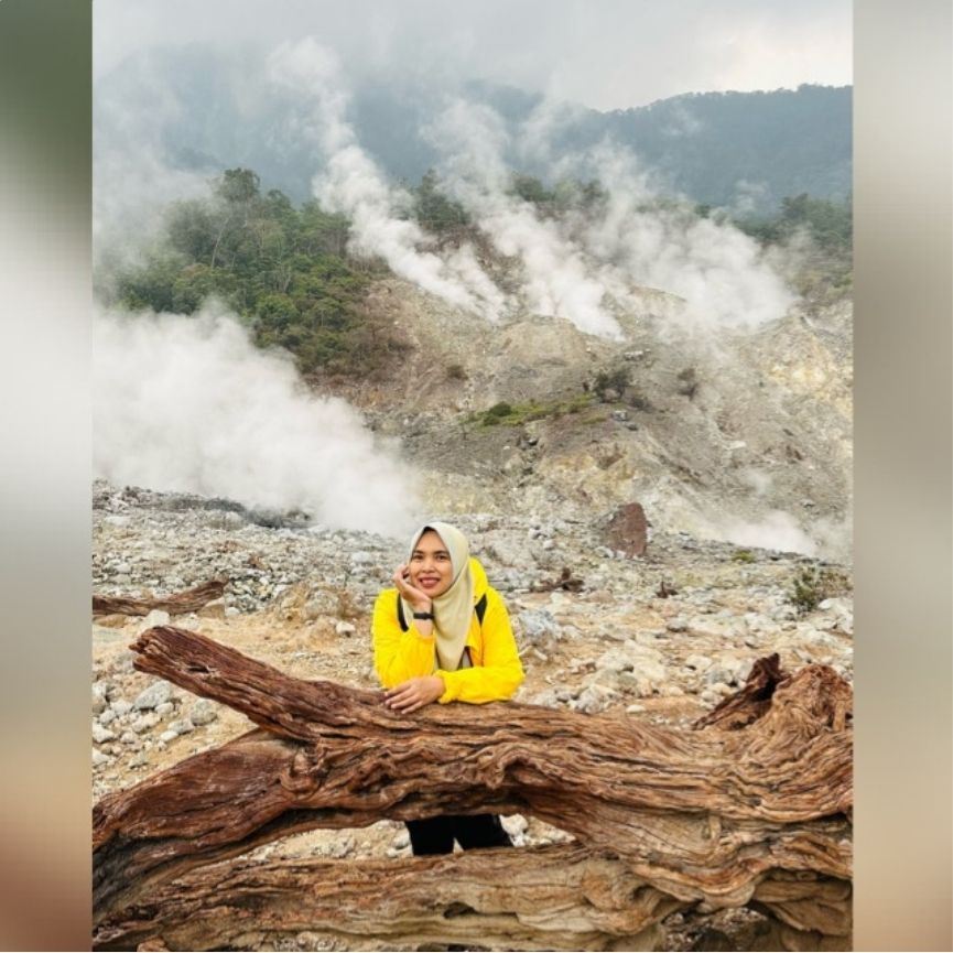 Person in a yellow jacket sitting on a log with steam in the background